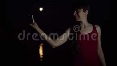 一个年轻的女人用智能手机相机对着红月自拍。